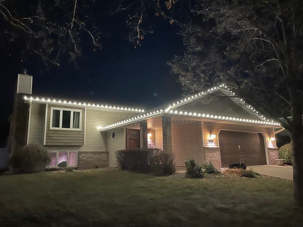 Modern home decorated with festive lights at night, showcasing architectural features and greenery.