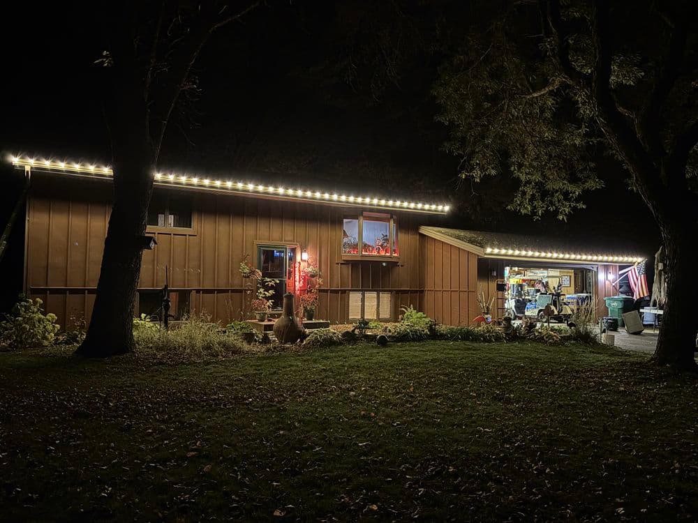 Cozy brown house with festive lights and decorations, surrounded by trees at night.